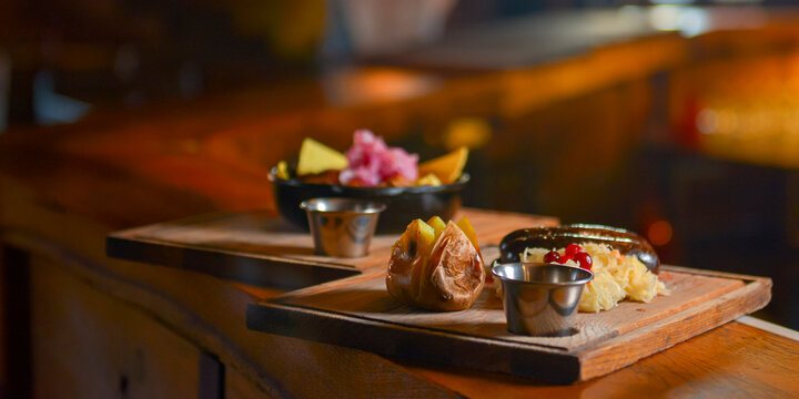 Baked potato with sausages and cabagge salad with sauce served on a wooden cutting board in a restaurant or cafe.