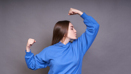 Portrait of cheerful young girl bending biceps isolated on gray background.