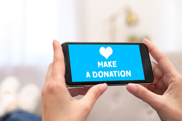 Woman holding smartphone with text MAKE A DONATION indoors, closeup