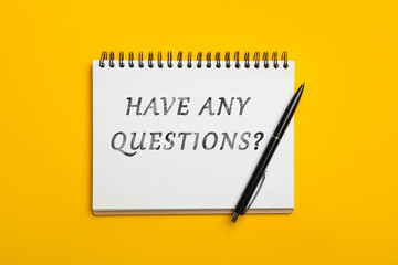 Open notebook with phrase HAVE ANY QUESTIONS and pen on yellow background, top view