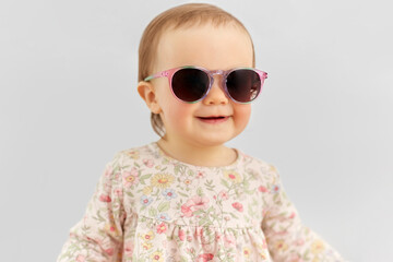 childhood, summer and people concept - happy little baby girl in sunglasses over grey background