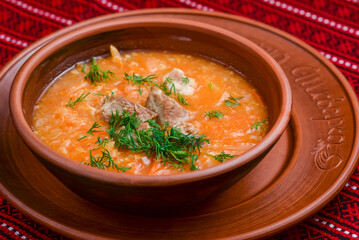 Chicken soup with vegetables and meat served in a white bowl over rustic wooden background with red...