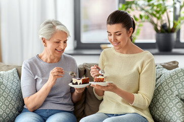 family, generation and people concept - happy smiling senior mother and adult daughter eating cake...