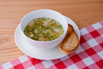 Chicken soup with vegetables and meat served in a white bowl over rustic wooden background with red plaid tablecloth.