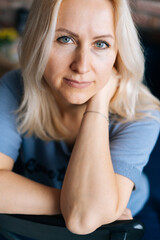 Close-up of face of blonde woman with perfect skin looking at camera. Portrait of lovely middle aged lady indoor.
