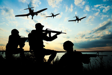 Fototapeta na wymiar Silhouettes of soldiers in uniform with assault rifles and military airplanes patrolling outdoors