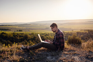 man with laptop sitting on the edge of a mountain with stunning views of the valley