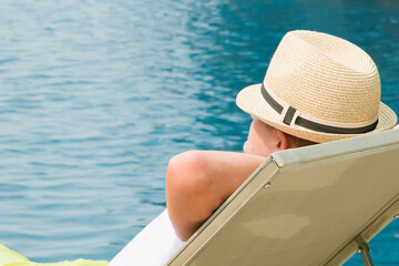 Boy on the longue chair near the swimming pool relaxing. Travel concept, travelling, hotel business.