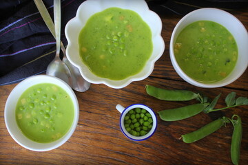 Fresh green pea soup with pea seeds and pea pods around , top view