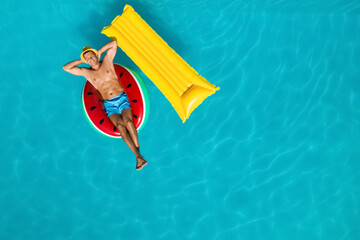 Happy man with inflatable mattress and ring in swimming pool, top view. Summer vacation