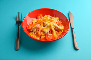 Melting cheddar cheese over the top of french fries covered in spicy sauce with meat and tomatoes. Blue background.
