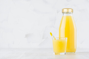 Fresh orange juice in glass bottle mock up with wine glass, straw on wood table in soft light white interior, template for packaging, advertising, design product, branding identity.