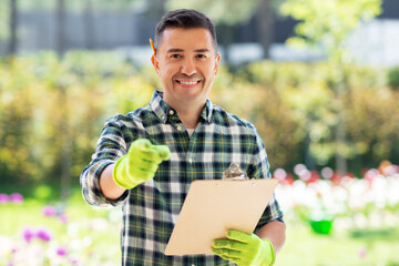 gardening and people concept - happy smiling middle-aged man with clipboard pointing finger to...