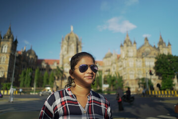 Obraz premium happy young woman in sunglasses. Young Indian Girl In front of Chhatrapati Shivaji Maharaj terminus (CSTM) Mumbai India