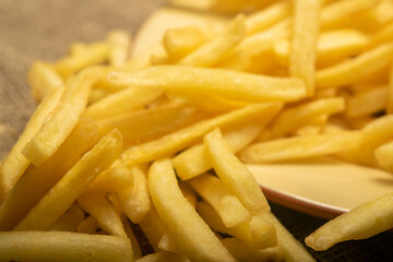 French fries in a round plate on a homespun cloth with a rough texture. Close up.