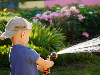 a small child in a cap watering the plants with a hose