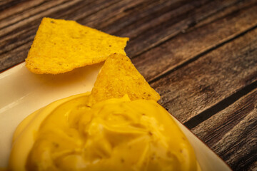 Corn chips with cheese sauce on a wooden background. Close up.