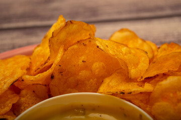 Potato chips on a round platter and a saucepan with cheese sauce. Close up.