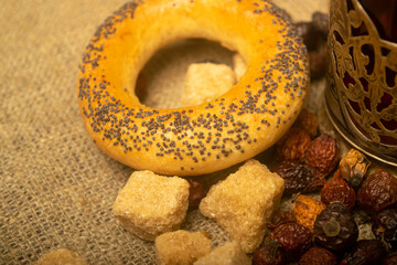 Small bagels, chunks of brown cane sugar and dried rosehip fruit scattered on a homespun cloth with a rough texture. Close up.