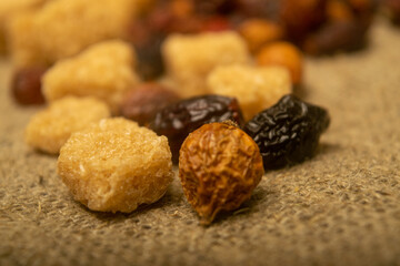 Pieces of brown cane sugar and dried rosehip fruit scattered on a homespun cloth with a rough...