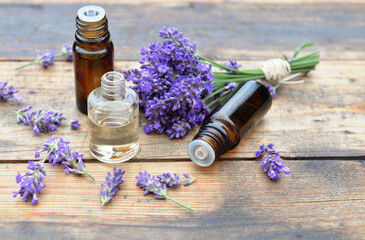 bottles of essential oil with one spilled on wooden background and bouquet of  lavender flowers