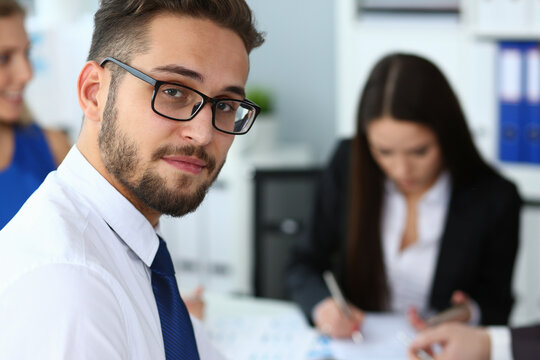 Portrait of cheerful young male clerc in glasses doing paper work with team of managers