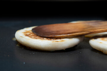 flipping the white utappam dosa on hot non stick tawa with wooden spatula