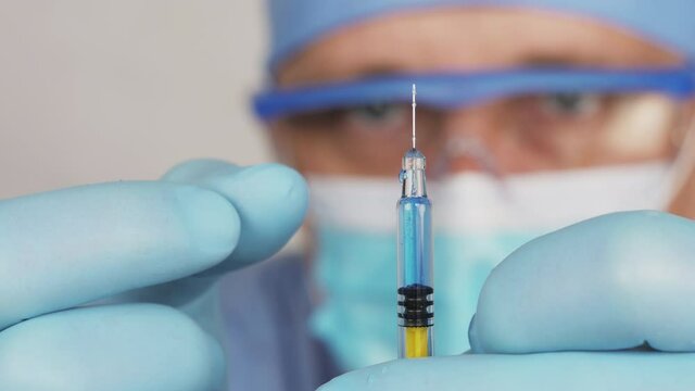 Vaccination. Syringe with a vaccine, medical solute in the hands of the doctor. Doctor in the medic face mask is preparing an injection. Close up view