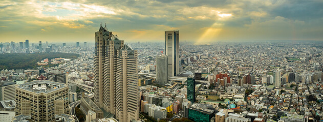 Warm colors panorama of Tokyo before sunset with dramatic cloudy orange sky and a sun rays seen from Tokyo Metropolitan Government Building (Shinjuku) in autumn, Japan.