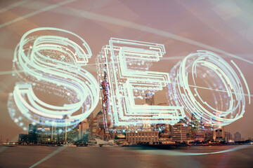 SEO hologram on city view with skyscrapers background double exposure. Search optimization concept.