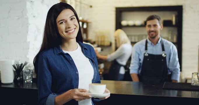 Handsome Caucasian barmen serving coffee to the pretty brunette woman at the bar, then she turning and smiling to the camera.