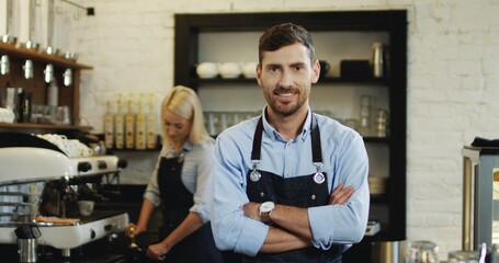 Portrait of male barista standing behind counter when young blond woman barista making coffee on the special machine