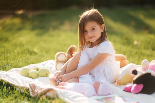 Adorable little girl sits on plaid outdoors and read book. Happy smiled baby girl spend time on back yard in sunset