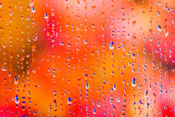 Jewel like drops of rainwater on the outside of a windowpane with vibrant autumn coloured leaves  providing a soft defocussed background.