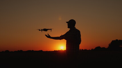 Silhouette A man lands a drone landing on his hand in nature at sunset