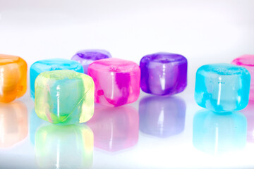 Colored ice cubes reflected in glass on a white background