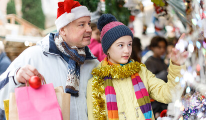 Happy teen girl with her loving father choosing Xmas decoration on outdoor market..