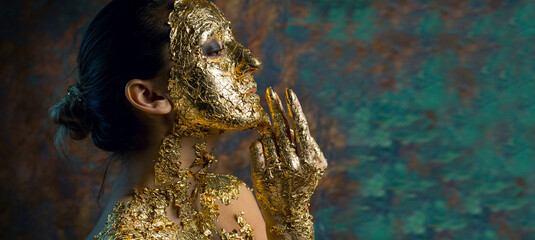 Girl with a mask on her face made of gold leaf. Gloomy studio portrait of a brunette on an abstract background.