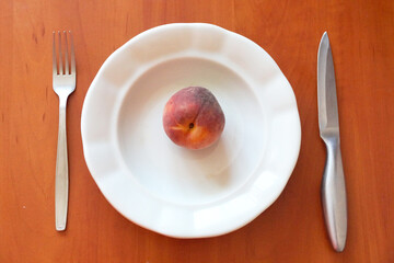 one peach on an empty white plate and cutlery nearby, healthy eating concept
