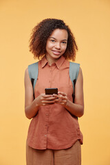 Portrait of smiling pretty Afro-American student girl in casual outfit communicating on social media using smartphone, studio shot
