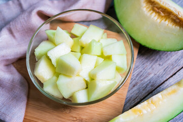 Cut of fresh sweet green melon in bowl glass on the wooden table. Fruits or healthcare concept. Selective focus, Top view.