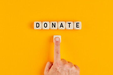 The word donate written on wooden cubes with a male hand pushing the button for donation. Charity...