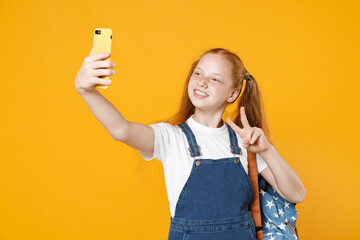 Young school girl 12-13 years old in white t-shirt backpack hold in hand using mobile cell phone doing selfie isolated on yellow background children studio portrait Kids education lifestyle concept