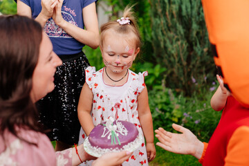 girl blows out candle on birthday cake on lawn