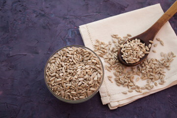 Sunflower seeds in a bowl and old wooden spoon on white serviette. Violet grunge background
