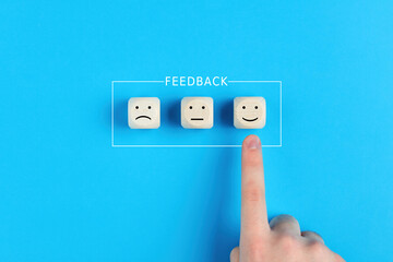Fototapeta premium Male hand chooses the happy face among unhappy faces on wooden blocks. Concept of customer satisfaction or positive feedback.