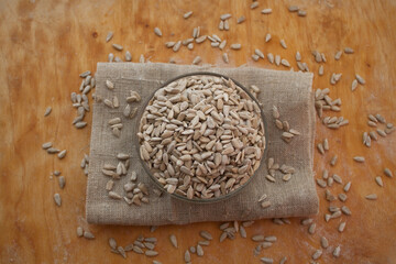 Sunflower seeds in a bowl on a sackcloth. Wooden background
