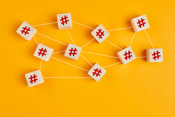 Hashtag symbols on wooden cubes connected to each other with lines on yellow background. Hashtag...