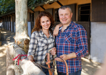 Mature positive family couple with belly-band standing at stable outdoor
