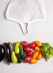 Eco-friendly mesh bag lies next to vegetables on a gray surface, copy space, flat lay, top view, zero waste concept.